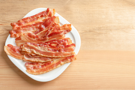 Plate with cooked bacon rashers on wooden tableの写真素材