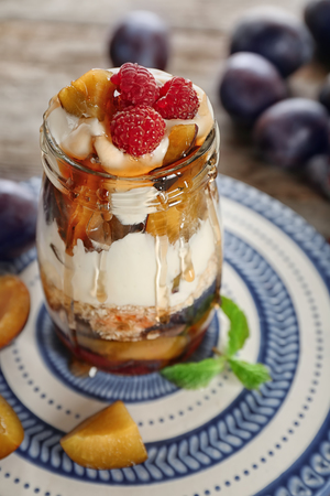 Oatmeal dessert with yogurt, raspberries and plums in jar on tableの写真素材