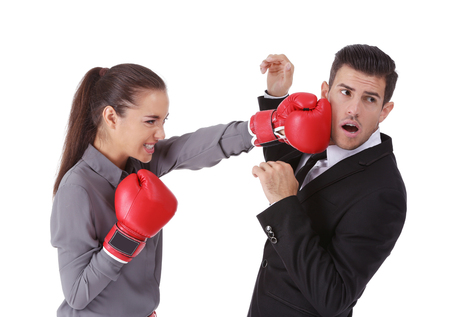 Woman in formal clothes and boxing gloves hitting businessman on white background