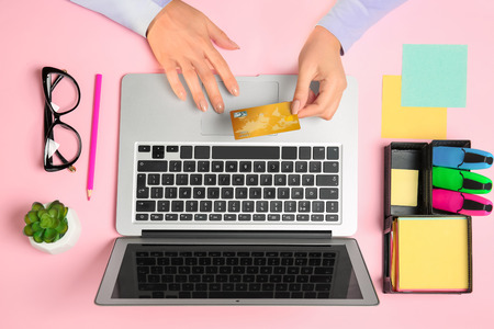 Young woman with credit card using laptop for online shopping on color background