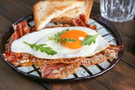 Plate with fried egg and bacon on wooden tableの写真素材