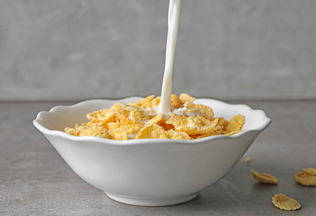 Pouring milk into plate with cornflakes on table