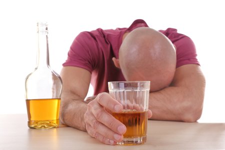 Drunk man sitting at table with whiskey against white background. Alcoholism conceptの写真素材