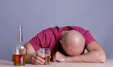 Drunk man sitting at table with whiskey. Alcoholism conceptの写真素材