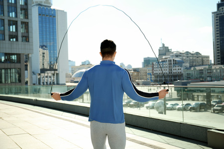 Sporty young man jumping rope outdoors