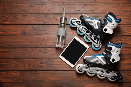 Roller skates, tablet computer and bottle of water on wooden background
