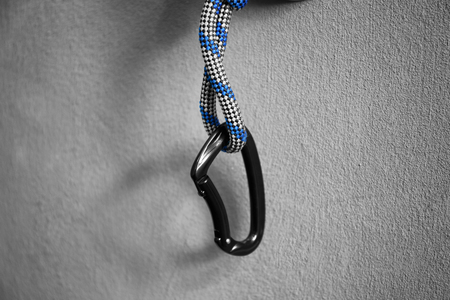 Rope with carabiner on grey wall, closeup