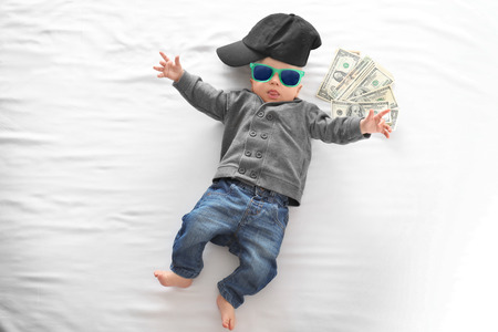 Cute boy with money on white bedsheet