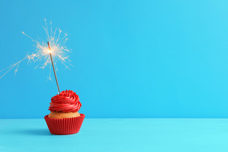 Tasty cupcake with sparkler on table against color backgroundの写真素材
