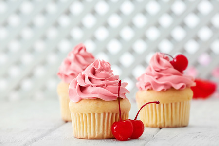 Delicious vanilla cupcakes and cherries on tableの写真素材