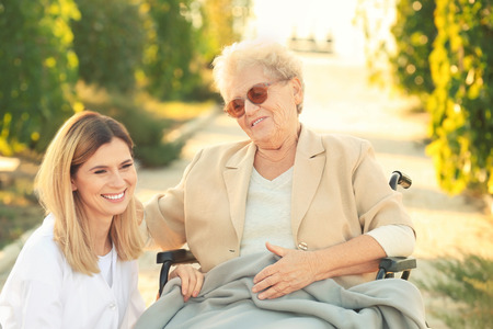 Senior woman in wheelchair and nurse from care home outdoorsの写真素材