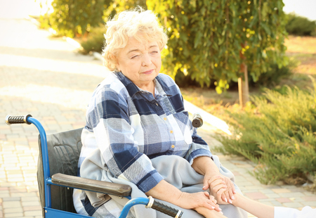 Senior woman in wheelchair holding hands of nurse from care home outdoorsの写真素材
