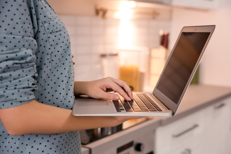 Woman using laptop in kitchenの写真素材