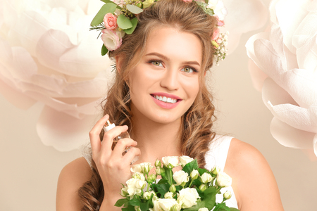 Beautiful young woman with bouquet and floral perfume on light backgroundの写真素材