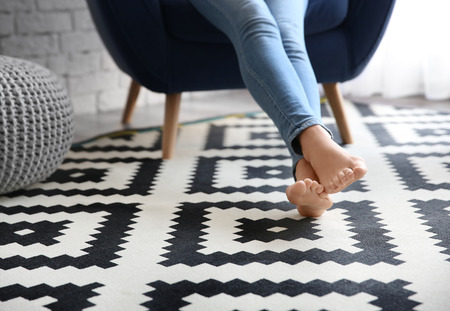 Woman sitting in armchair with feet on carpet at homeの写真素材