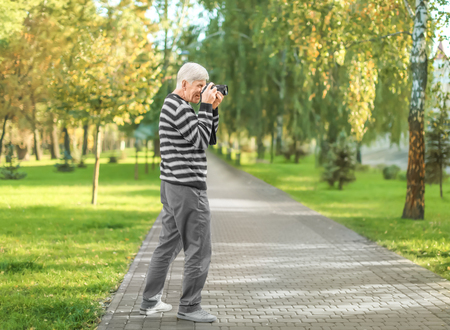 Stylish mature man taking photo in autumn park