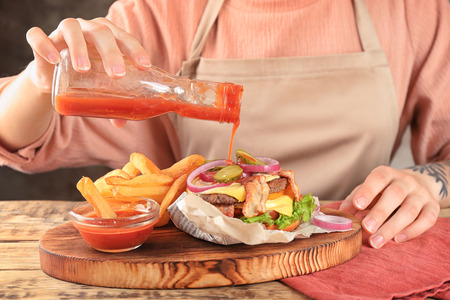 Woman pouring tomato sauce on double burgerの写真素材