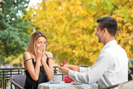 Young man with engagement ring making proposal of marriage to his girlfriend in cafeの写真素材