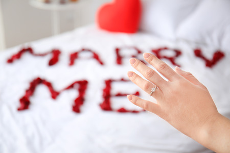 Woman accepting marriage proposal and wearing engagement ring in bedroomの写真素材