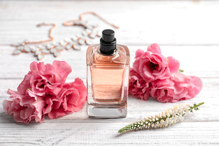 Bottle of perfume and fresh flowers on wooden background
