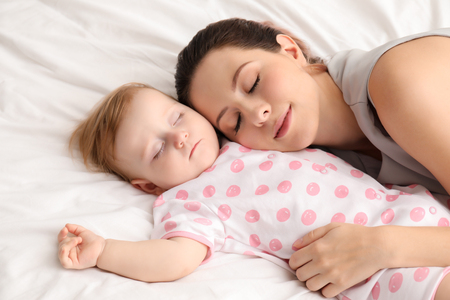 Young mother and her baby sleeping on bedの写真素材