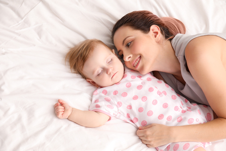 Young mother and her sleeping baby on bedの写真素材