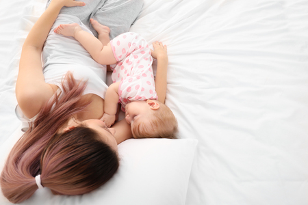 Young mother with her cute baby on bedの写真素材