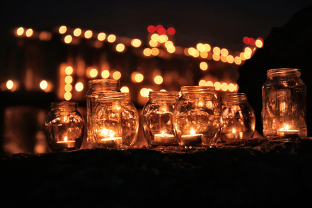 Jars with burning candles on blurred lights background at night