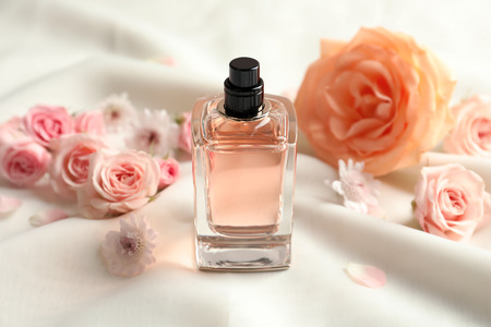 Bottle of perfume with flowers on light cloth