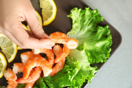 Woman holding tasty shrimp over plate on tableの写真素材