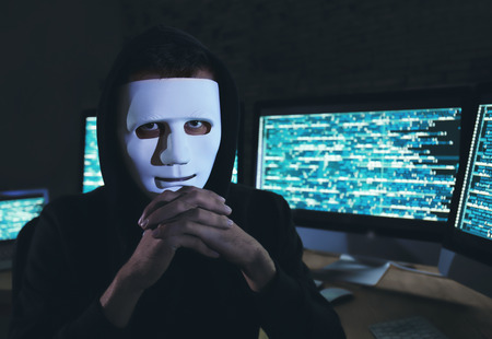 Masked hacker in dark room with computers. Threat of cyber attackの写真素材