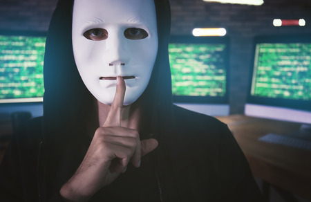 Masked hacker in dark room with computers. Threat of cyber attackの写真素材