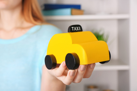 Woman holding yellow toy taxi cab, indoorsの写真素材