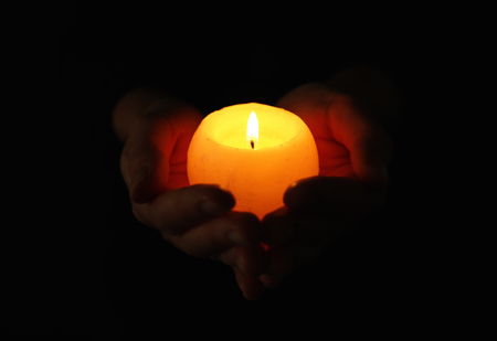 Young woman holding burning candle in darknessの写真素材
