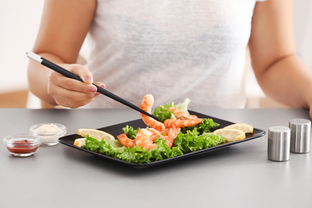 Young woman eating shrimps at tableの写真素材