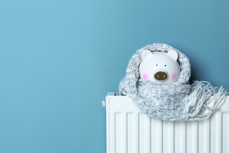 Piggy bank with warm scarf on heating radiator near color wallの写真素材