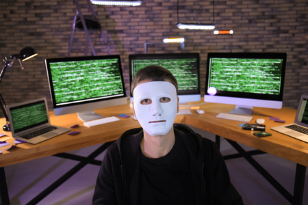 Masked hacker in dark room with computers. Threat of cyber attack