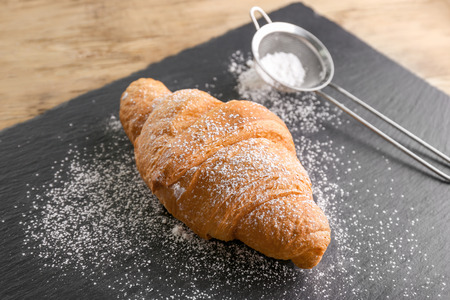Fresh yummy croissant with sugar powder on slate plateの写真素材