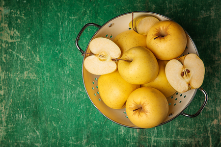 Colander with ripe yellow apples on green wooden background, top viewの写真素材