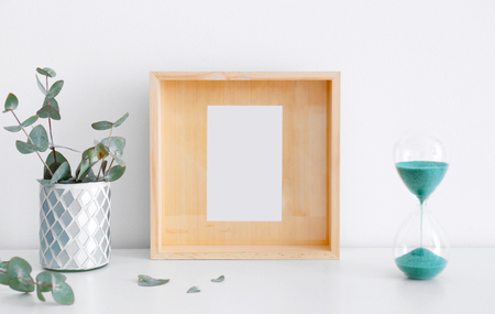 Empty wooden frame, hourglass and eucalyptus on table near white wallの写真素材