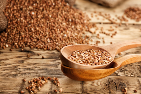Raw buckwheat and wooden spoons on tableの写真素材
