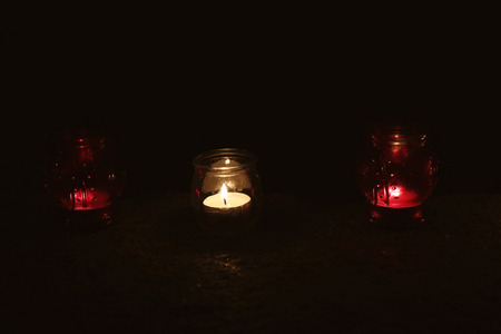 Jars with burning candles on stone surface in darkness