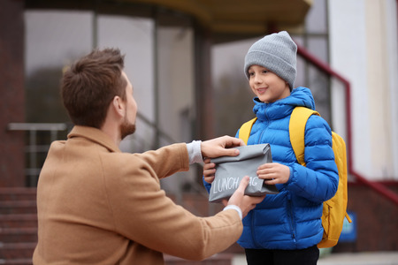 Young man giving lunch bag to his son in front of school