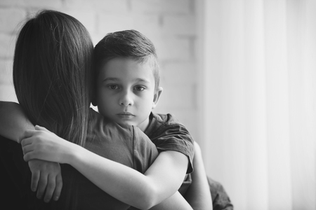 Sad little boy hugging his mother indoors, black and white effectの写真素材