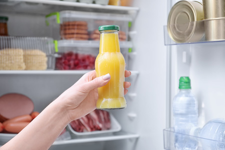 Woman holding bottle of juice near open refrigerator, closeupの写真素材