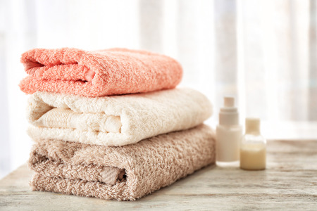 Bath towels and cosmetics on table against light backgroundの写真素材