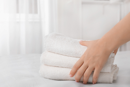 Woman putting stack of towels on bedの写真素材