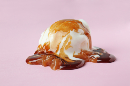 Ice cream ball with caramel sauce on color backgroundの写真素材