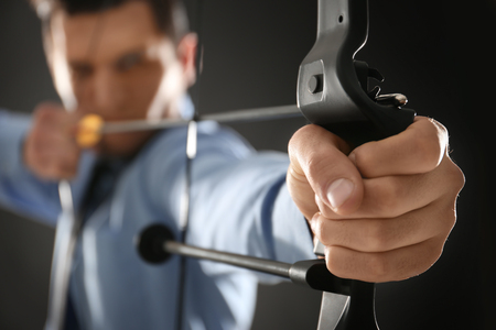 Young businessman practicing archery on dark background