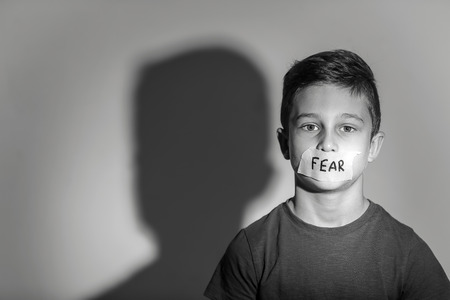 Sad little boy with taped mouth and word "Fear" on grey background, black and white effectの写真素材